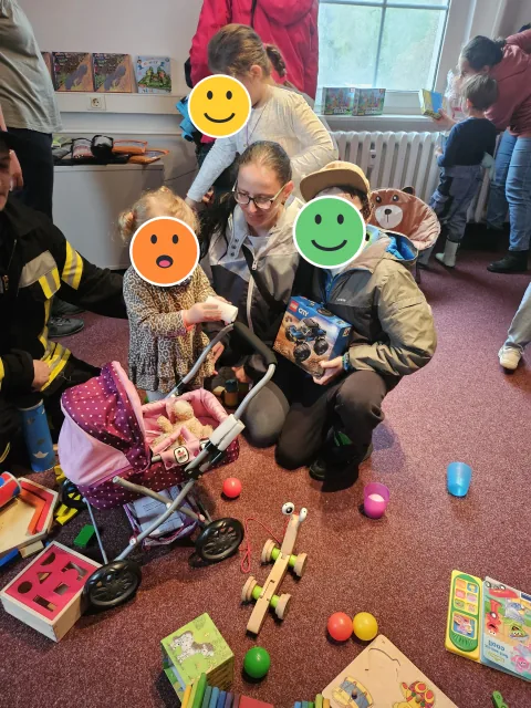 Kinder und Erwachsene an der Spielecke; die Kindergesichter sind mit Smileys verdeckt
