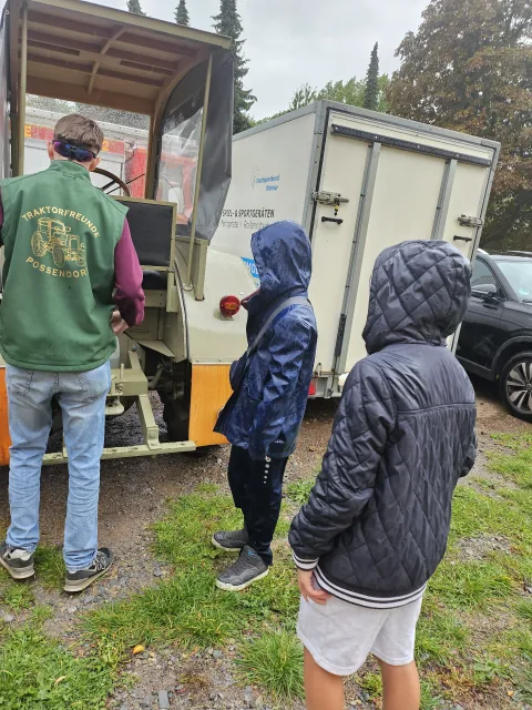 Kinder betrachten gemeinsam mit einem Helfer einen Traktor von hinten