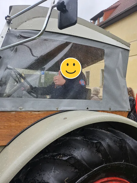 Kind am Steuer eines Traktors; das Gesicht ist mit einem Smiley verdeckt